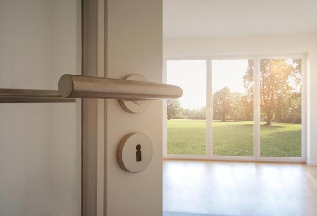 Sunlit empty living room with glass doors opening to a lawn